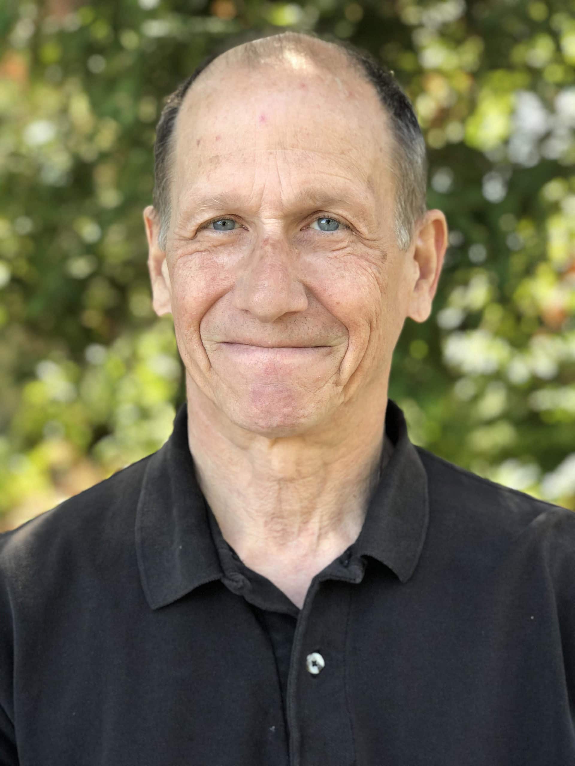 Smiling man in a black shirt stands outdoors.