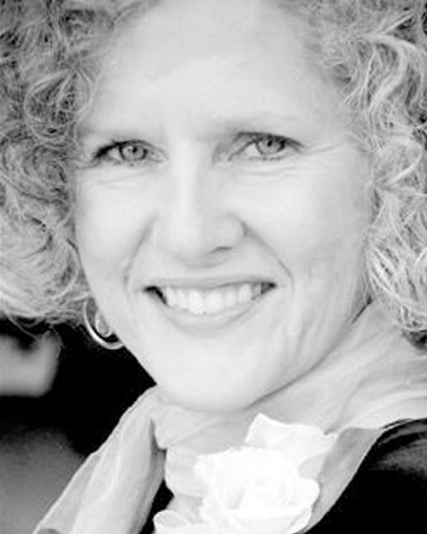 A close up of a woman's face who has very curly blond hair, smiling.